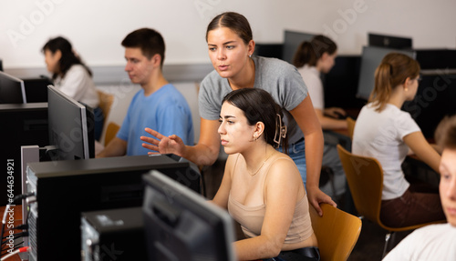 Schoolgirl using computer and teacher helping to him in classroom