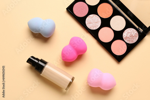 Set of makeup sponges, liquid foundation and eyeshadows on color background