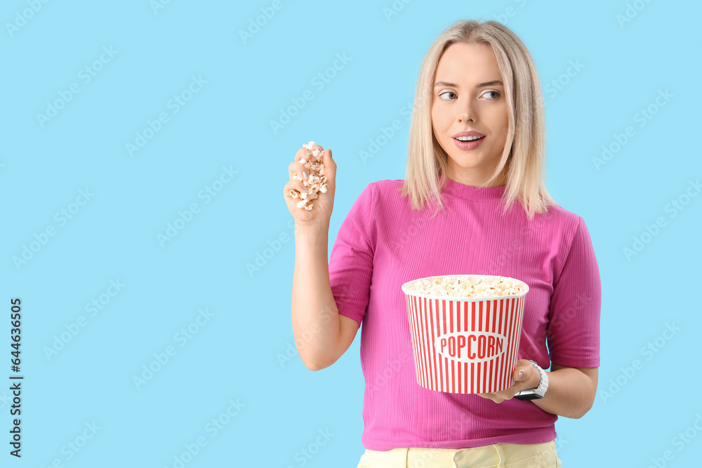 Thoughtful young beautiful woman with bucket of popcorn on blue background Thoughtful young beautiful woman with bucket of popcorn on blue background