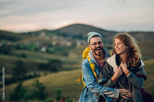 Couple of hikers hugging and walking along mountain grassy trail during a vacation