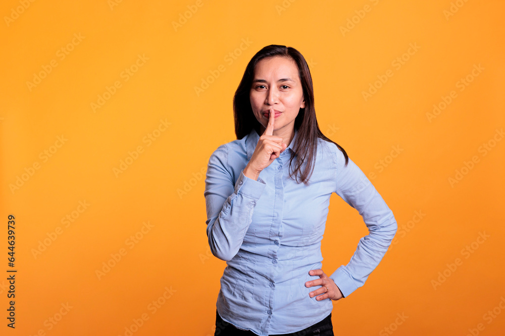 Portrait of filipino woman making silence gesture by putting forefinger over lips posing over yellow background. Silent woman shushing people indicating secrecy and confidentiality. Portrait of filipino woman making silence gesture by putting forefinger over lips posing over yellow background. Silent woman shushing people indicating secrecy and confidentiality.