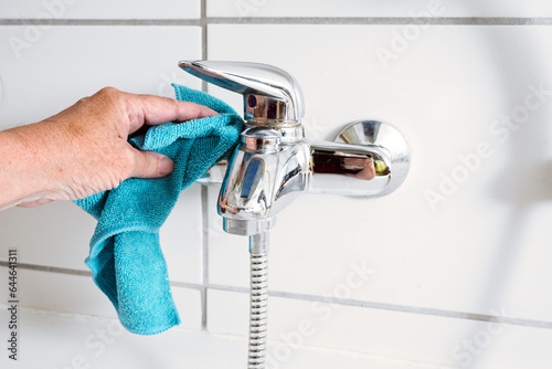Cleaning a bathtub faucet with a blue microfiber cloth to remove limescale stains from hard calcium water, copy space, selected focus, narrow depth of field
