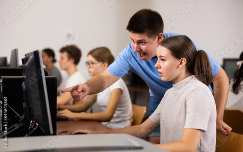 Excited male teenager giving a clue to the female co-learner while she is using pc in the computer classrooms