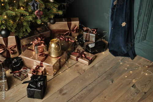 Fototapeta Naklejka Na Ścianę i Meble -  Close-up black and gold gift boxes under a Christmas tree on a wooden floor. Stylish packaging