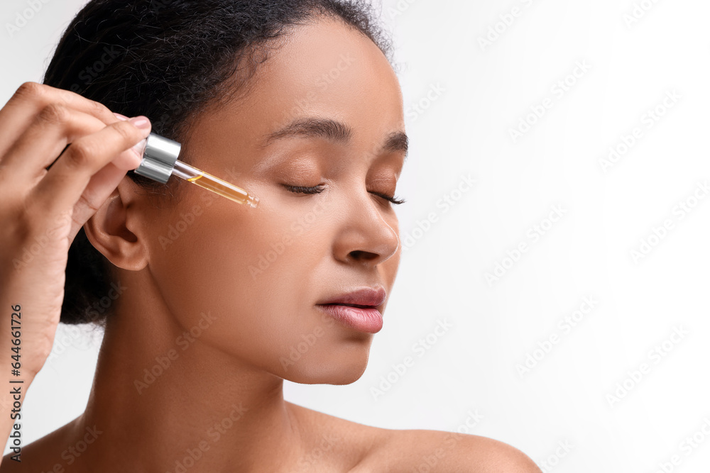 Beautiful woman applying serum onto her face on white background, closeup. Space for text