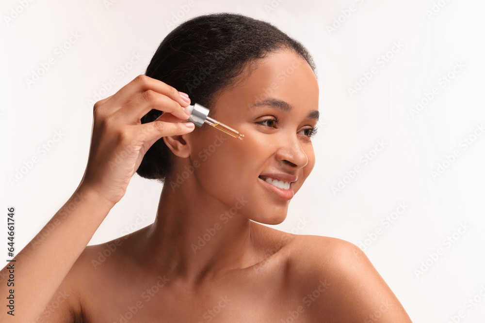 Fototapeta premium Smiling woman applying serum onto her face on white background