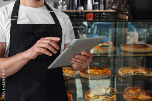 Seller with tablet near showcase in bakery shop, closeup. Space for text