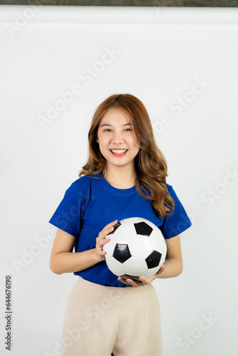 Happy Asian female soccer fan sending support to favorite team with soccer ball, smiling woman in blue t-shirt holding soccer ball to cheer at soccer game, isolated on white background. © ArLawKa