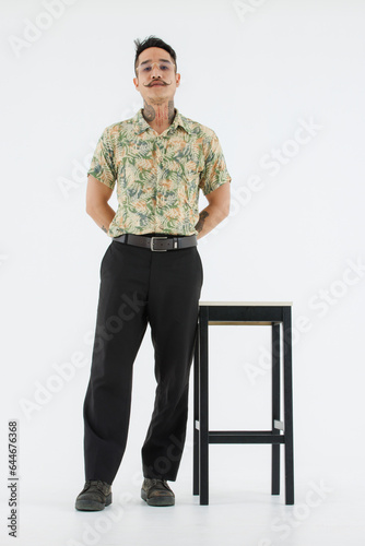 Isolated cutout studio full body shot Asian vintage classic male fashion model with mustache neck arm tattoo wearing eyeglasses in casual outfit standing near chair with boots on white background