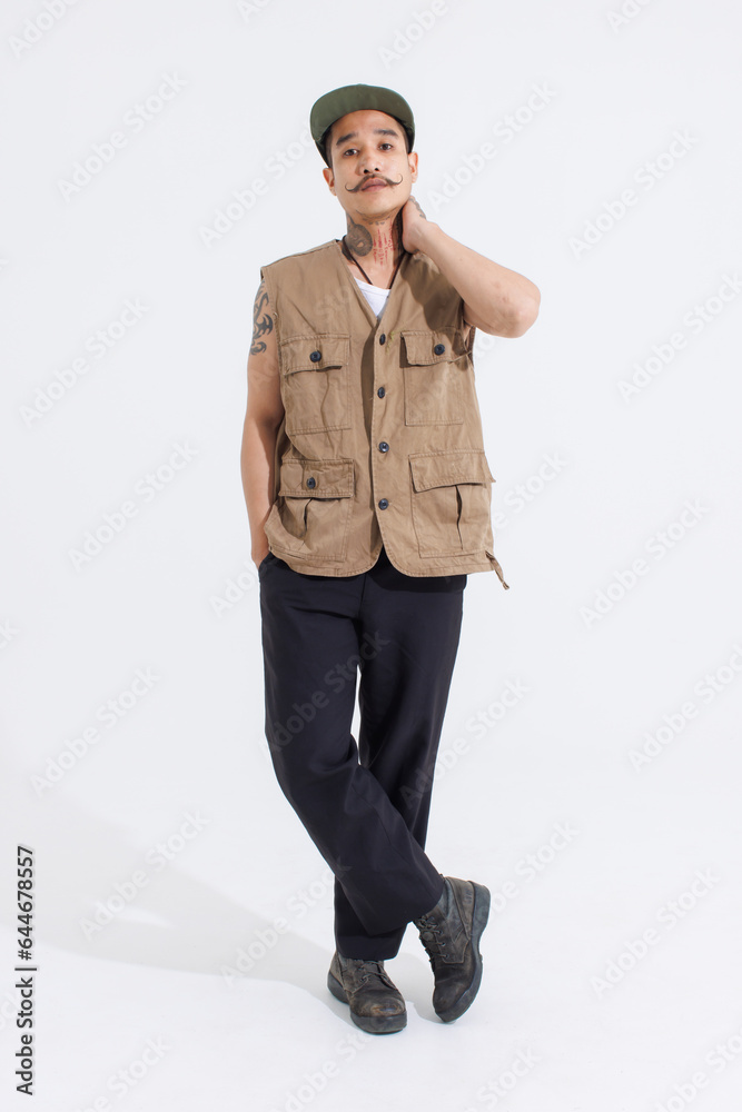 Portrait isolated cutout studio full body shot Asian vintage classy mustache neck arms tattoos male fashion model in casual fashionable safari vest and cap standing look at camera on white background Portrait isolated cutout studio full body shot Asian vintage classy mustache neck arms tattoos male fashion model in casual fashionable safari vest and cap standing look at camera on white background