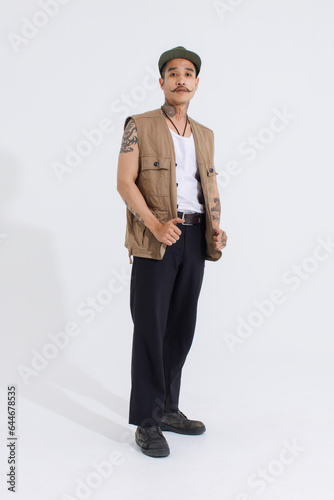Portrait isolated cutout studio full body shot Asian vintage classy mustache neck arms tattoos male fashion model in casual fashionable safari vest and cap standing look at camera on white background