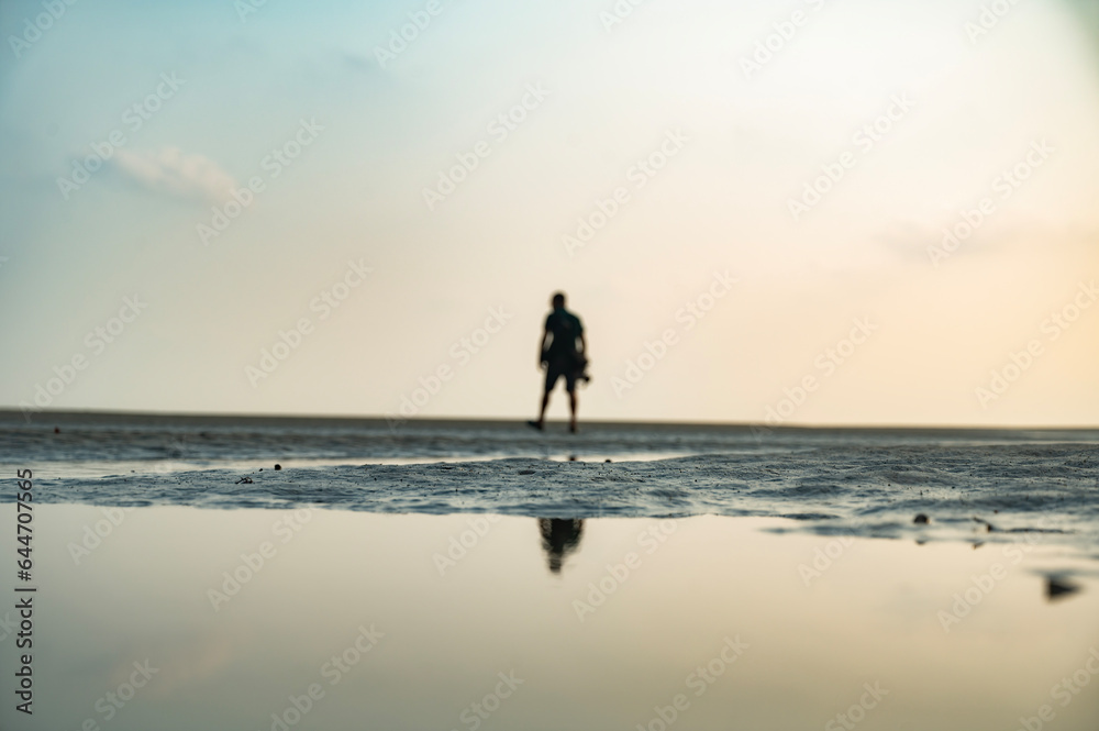 calm man walking in the sand. Man goes to the sea on dark sand beach under sunset sky.