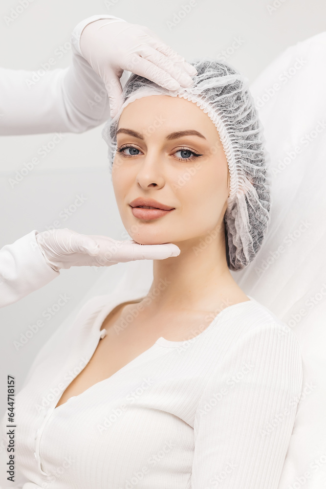 A beautiful, young woman with well-groomed, smooth skin on a light background. Gloved hands touch the woman's face. A beautiful, young woman with well-groomed, smooth skin on a light background. Gloved hands touch the woman's face.