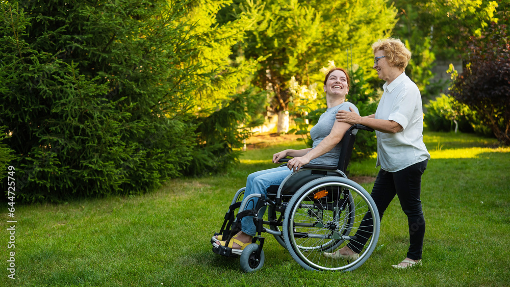 An elderly woman is carrying an adult daughter sitting in a wheelchair. Walk outdoors. An elderly woman is carrying an adult daughter sitting in a wheelchair. Walk outdoors.