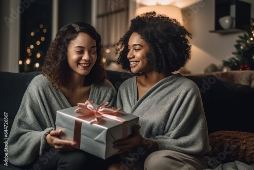 lesbian couple giving gifts and presents to each other, female gay lgbt homosexual african american marriage or black girlfriends having a good time indoors on christmas eve or new year night