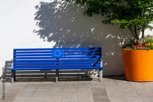 Europe: Blue bench with euopean flag (yellow stars on blue) next to a big orange flower pot with flowers and a japaneese tree photo