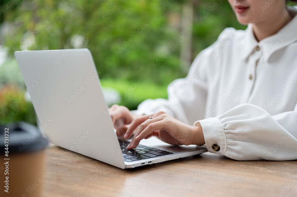 Close-up image of a woman typing on laptop keyboard, working on her laptop at a table outdoors. Close-up image of a woman typing on laptop keyboard, working on her laptop at a table outdoors.