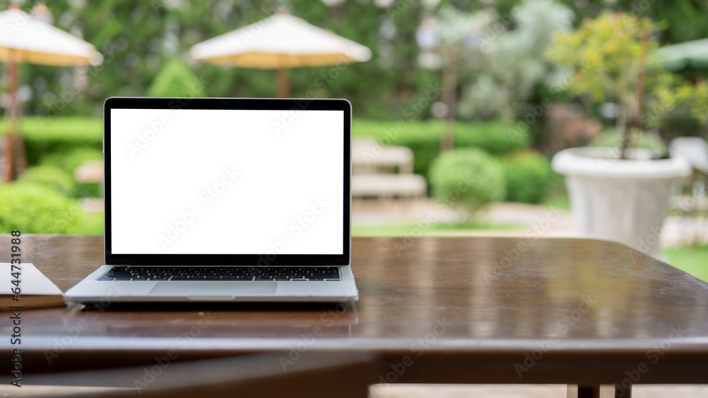 A laptop mockup on a table in a cafe with a blurred beautiful greenery garden in the background. A laptop mockup on a table in a cafe with a blurred beautiful greenery garden in the background.