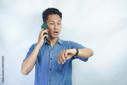 Young asian businessman wearing blue shirt worried looking at his watch. man is on the phone and looking at his watch