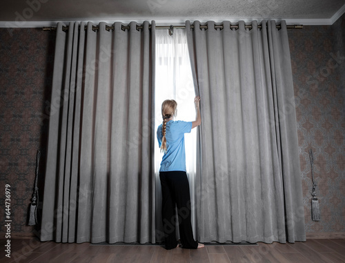 Girl at home opens the curtains and looks out the window