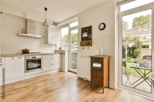 a kitchen with wood flooring and white cabinetd doors leading to an open patio door that leads out onto the back yard photo