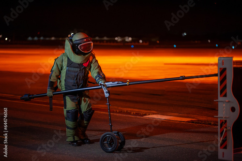 Bomb disposal officers wearing protective gear Investigating a suspected bomb outside the airport building. with remote robotic arm