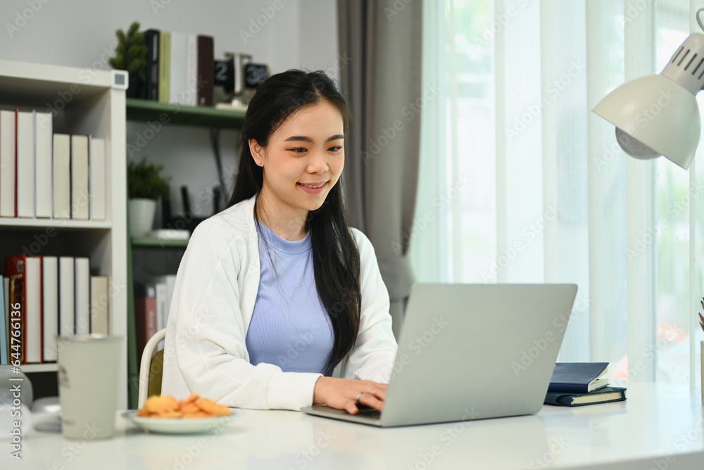 Smiling young woman using laptop at home, sending email or browsing internet. People and technology concept Smiling young woman using laptop at home, sending email or browsing internet. People and technology concept