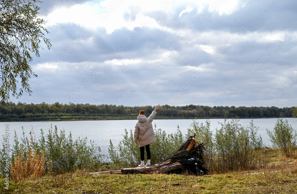 A girl in a light jacket and a brown hat looks at the autumn landscape A girl in a light jacket and a brown hat looks at the autumn landscape