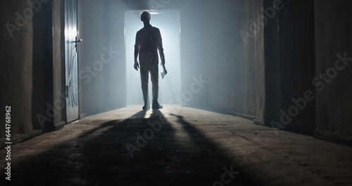 Maniac carrying a murderous weapon escaping from crime scene. Bloodthisty criminal carrying an axe in hallway of old house 