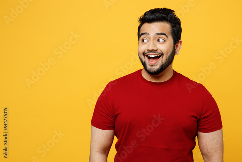Young surprised shocked astonished amazed stunned happy Indian man he wears red t-shirt casual clothes look aside on area isolated on plain yellow orange background studio portrait. Lifestyle concept. photo