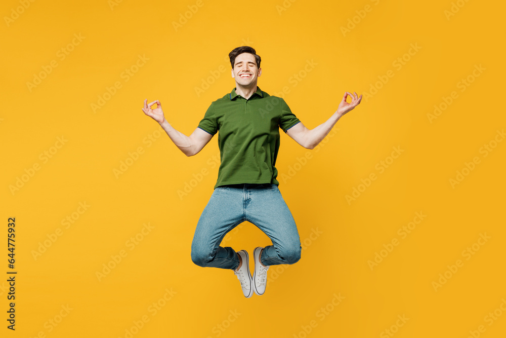 Full body young spiritual man wears green t-shirt casual clothes jump high hold spread hands in yoga om aum gesture relax meditate try to calm down isolated on plain yellow background studio portrait.