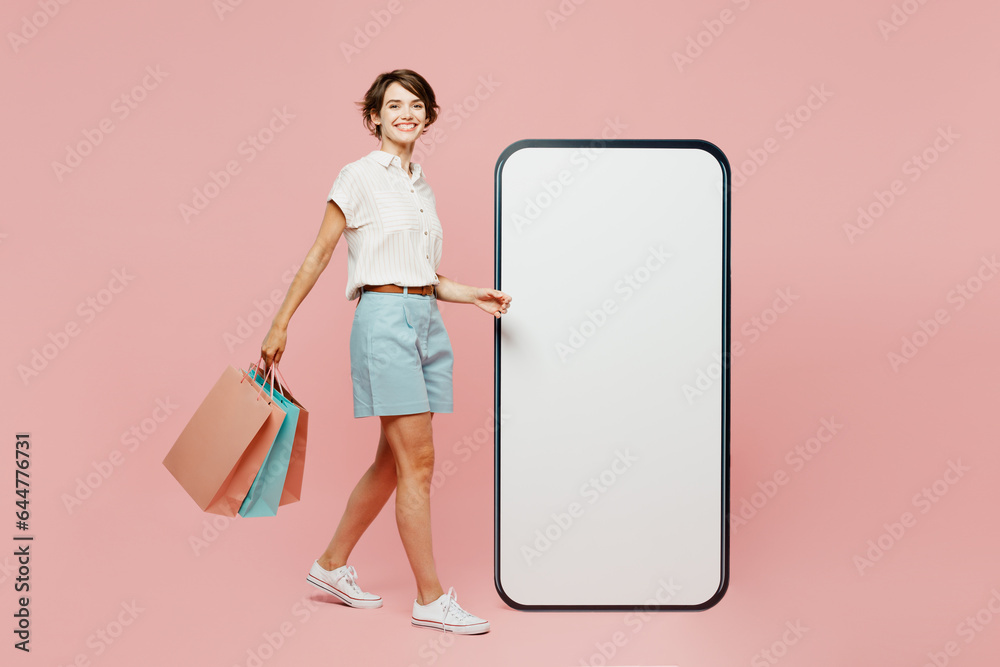 Full body young woman wear casual clothes hold shopping package bags big huge blank screen area mobile cell phone look camera isolated on plain pink color background Black Friday sale buy day concept