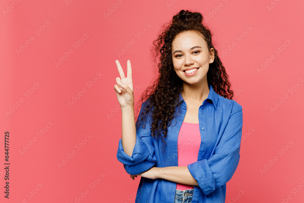Young smiling happy cheerful woman of African American ethnicity she wear blue shirt casual clothes showing victory sign look camera isolated on plain pastel pink background studio. Lifestyle concept. Young smiling happy cheerful woman of African American ethnicity she wear blue shirt casual clothes showing victory sign look camera isolated on plain pastel pink background studio. Lifestyle concept.