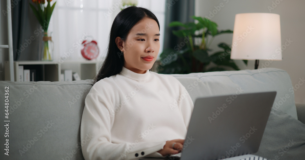 Asian woman using a laptop computer while sitting on the sofa Asian woman using a laptop computer while sitting on the sofa
