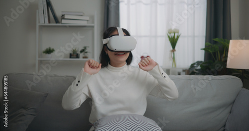Asian woman watching a concert via VR glasses and dancing while sitting on the sofa © Johnstocker