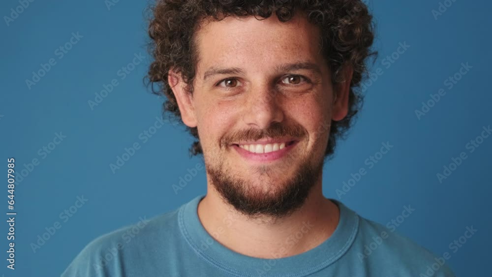 Close-up, man raising his head and looking at the camera with smile isolated on blue background