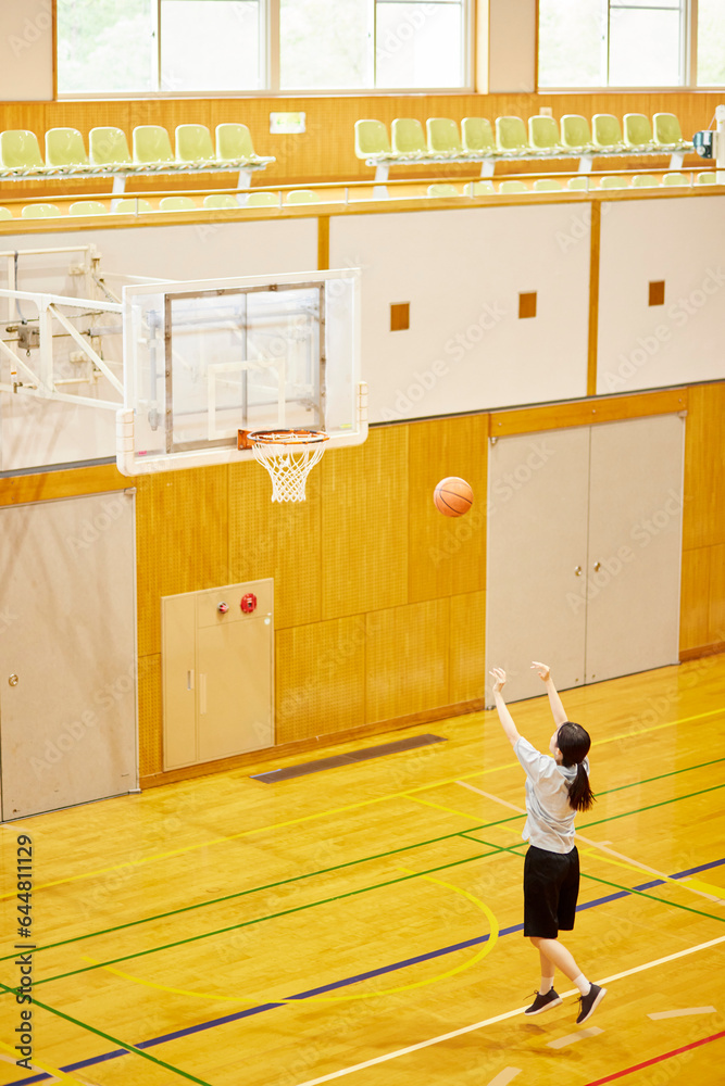 Obraz premium 体育館でバスケットボールの練習をするスポーツウェアを着た日本人女性
