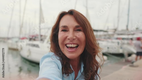 Close up, lovely middle aged woman sitting in port making video call from mobile phone