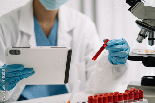 Doctor taking a blood sample tube from a rack with machines of analysis in the lab background, Technician holding blood tube test in the research laboratory.