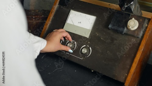 A female scientist using a vintage fluorometer. The woman is turning knobs and dials on the science equipment in a laboratory. photo