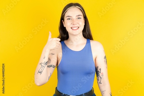Beautiful woman wearing blue tank top doing happy thumbs up gesture with hand. Approving expression looking at the camera showing success.