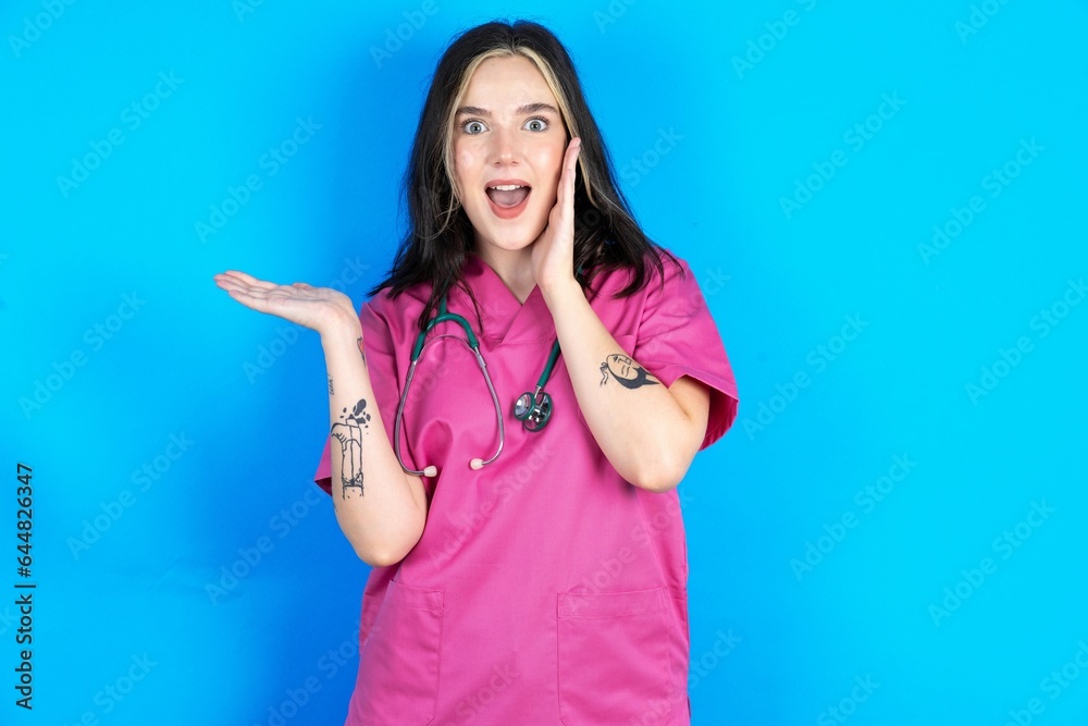 Fototapeta premium Crazy Young caucasian doctor woman wearing pink medical uniform advising discount prices hold open palm new product