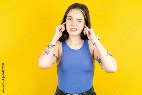 Beautiful woman wearing blue tank top covering ears with fingers with annoyed expression for the noise of loud music. Deaf concept.