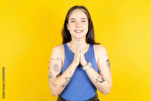 Beautiful woman wearing blue tank top praying with hands together asking for forgiveness smiling confident.