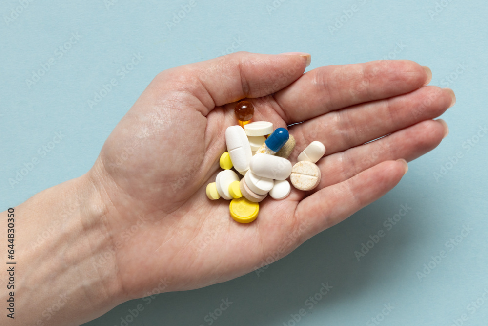 Woman's hand with medical pills on pastel blue background. Medical treatment for disease flu virus. Close-up pharmacy or health care concept. Woman's hand with medical pills on pastel blue background. Medical treatment for disease flu virus. Close-up pharmacy or health care concept.