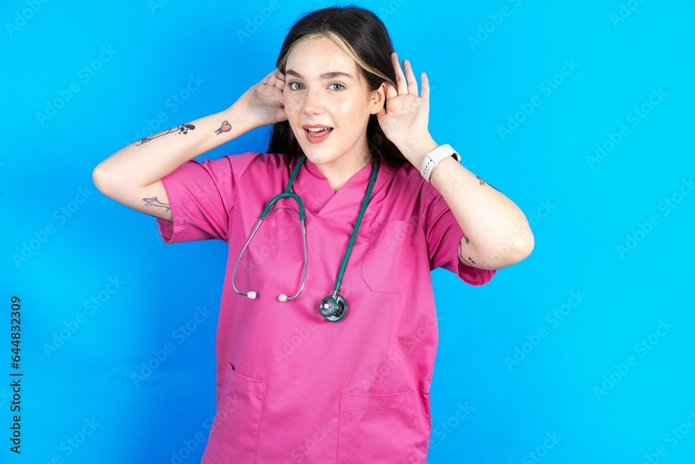 Young caucasian doctor woman wearing pink medical uniform Trying to hear both hands on ear gesture, curious for gossip. Hearing problem, deaf