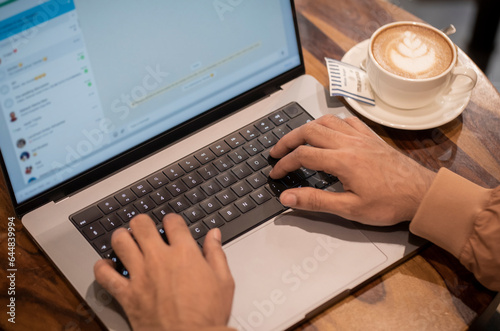 Quadro su tela A guy is typing in a chat on laptop and coffee cup and saucer kept aside on wood