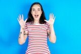 Delighted positive beautiful young woman wearing striped T-shirt opens mouth  and arms palms up after having great result