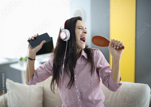 Woman with headphones and comb in her hands sings emotionally. Stress relief while singing concept