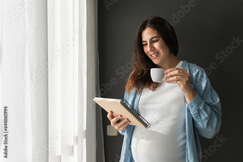 Smiling pregnant woman standing with notebook at home